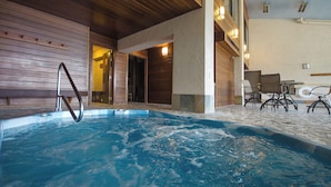 Una piscina interior con una terraza de madera y un área de descanso con sillas.