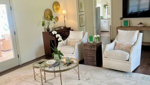 A living room with a ceiling fan, two white armchairs, a glass coffee table, and a TV mounted on the wall. - Prime Location Masters Rental - Only 2.2 miles from course in Augusta, GA! (Augusta)