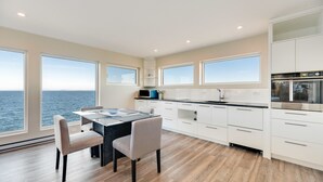 A modern kitchen with large windows, a dining area, and a view of the sea. - Orca View Suite 10 Mile Point (Victoria)