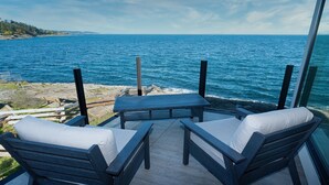 A balcony with a table and two chairs, overlooking a rocky shoreline and the sea. - Orca View Suite 10 Mile Point (Victoria)
