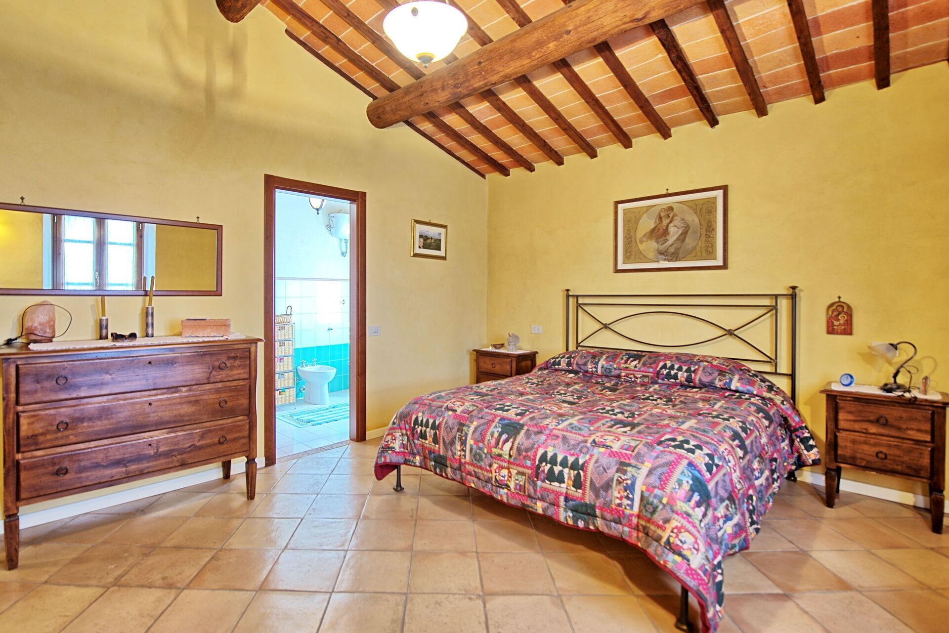 A bedroom with a wooden bed, a dresser, a nightstand, and a door leading to a bathroom.