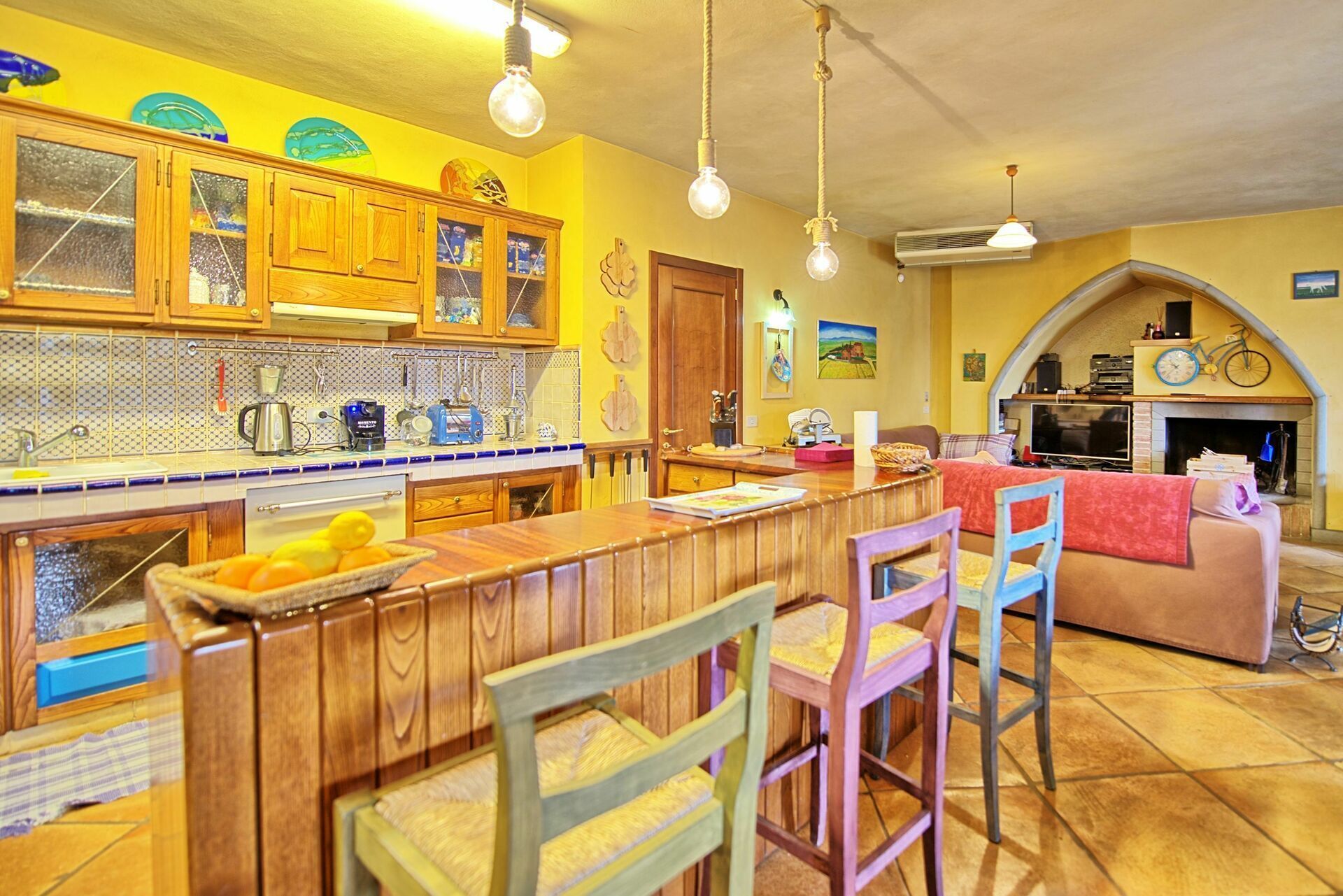 A kitchen with wooden cabinets, a central island with bar stools, and a dining area with a sofa and chairs.