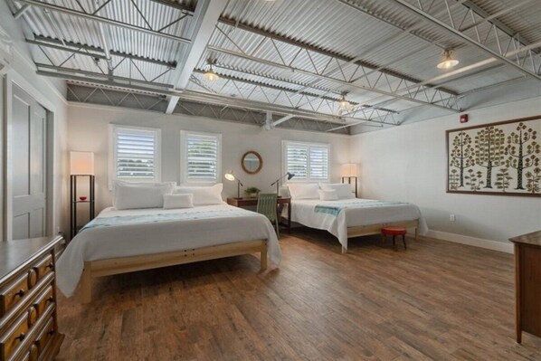 A bedroom with two beds, wooden flooring, and a high ceiling with metal beams.