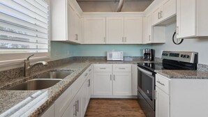A kitchen with white cabinets, granite countertops, a stainless steel sink, a microwave, a coffee maker, and a stove.