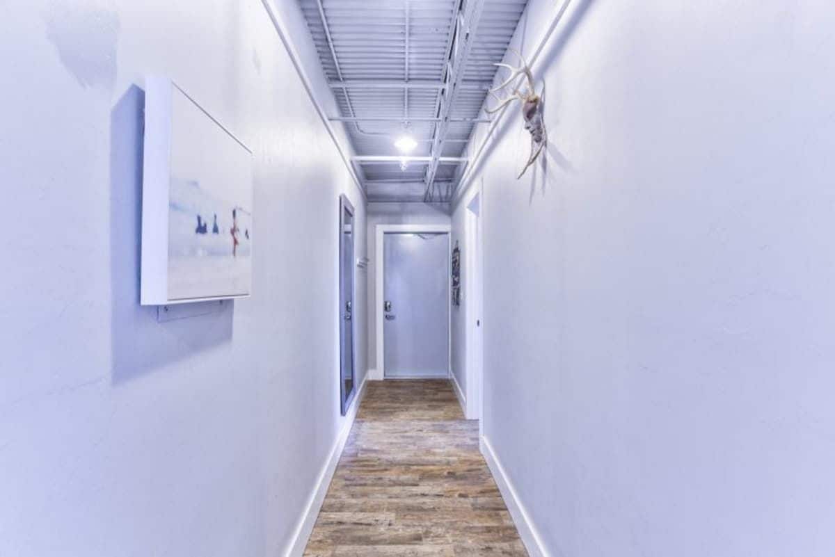 A hallway with white walls, a wooden floor, and a mounted antler on the right wall.