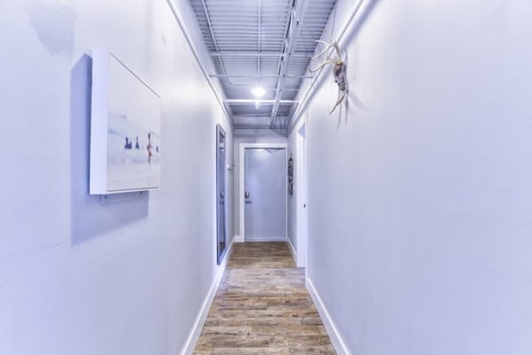 A hallway with white walls, a wooden floor, and a mounted antler on the right wall.