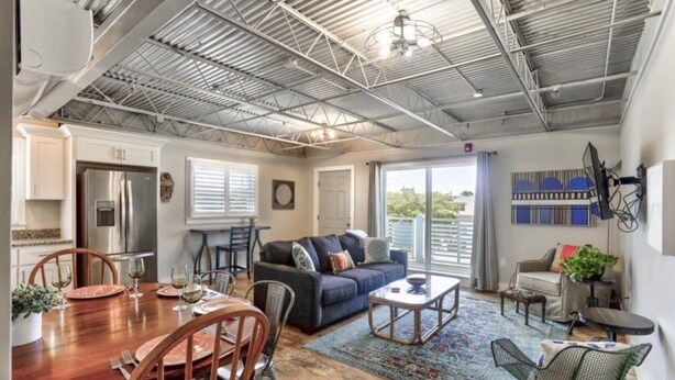 A spacious living area with a high ceiling, a dining table set for a meal, a sofa, and a television mounted on the wall.