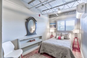 A bedroom with a bed, a chair, a dresser, a mirror, and a window with blinds.