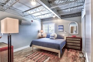 Relax in this stylish bedroom with a comfortable bed, nightstand, and dresser, plus a large window with blinds.