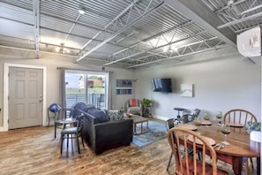 A spacious living area with a high ceiling, a dining table set for four, and a comfortable seating arrangement.