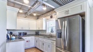 A modern kitchen with white cabinets, stainless steel appliances, and a wooden floor.