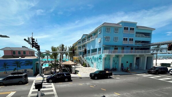 Un hotel de varios pisos con balcones, una zona de piscina y vista a la calle con coches y semáforos.