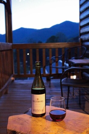 A bottle of Biltmore wine and a glass on a wooden table on a balcony with a view of mountains.