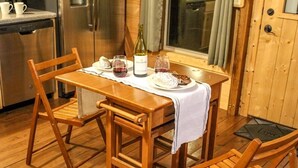 A wooden dining table with a white tablecloth, two wooden chairs, a bottle of wine, glasses, and a plate of food. - Turkey Trot- New Cabin in Black Mountain w/ views & discount Biltmore tickets! (Black Mountain)