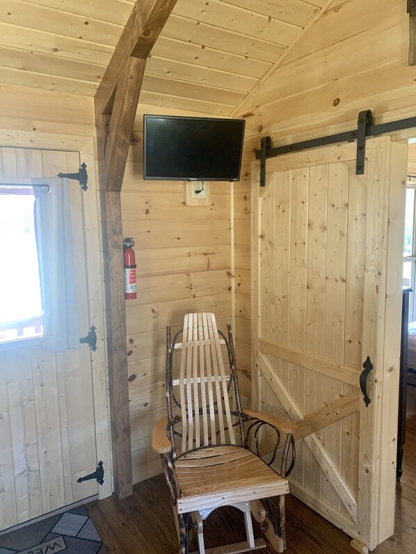 A wooden cabin interior with a wooden chair, a television mounted on the wall, and a sliding barn-style door.