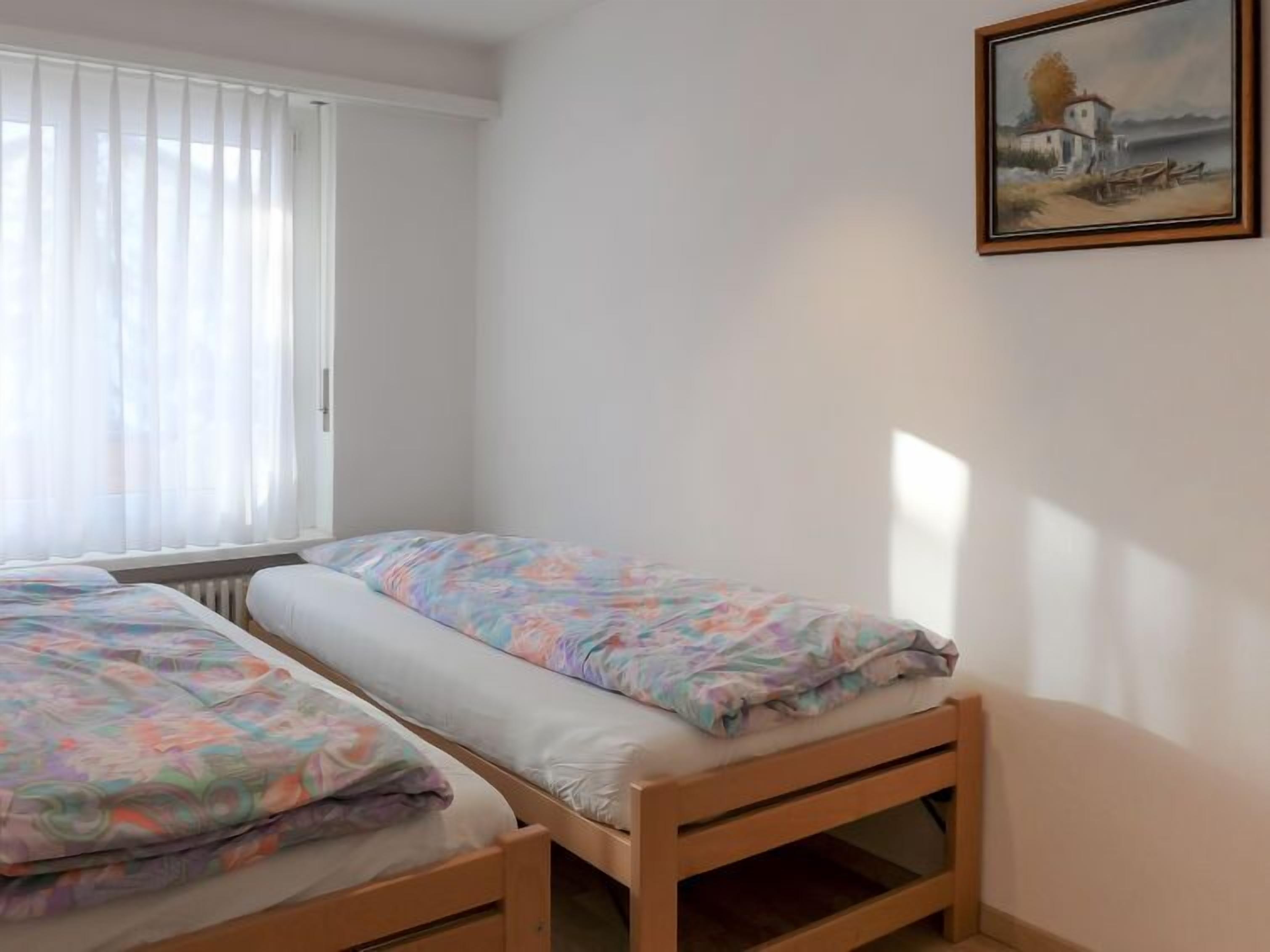 A bedroom with two single beds, a window with blinds, and a painting on the wall.