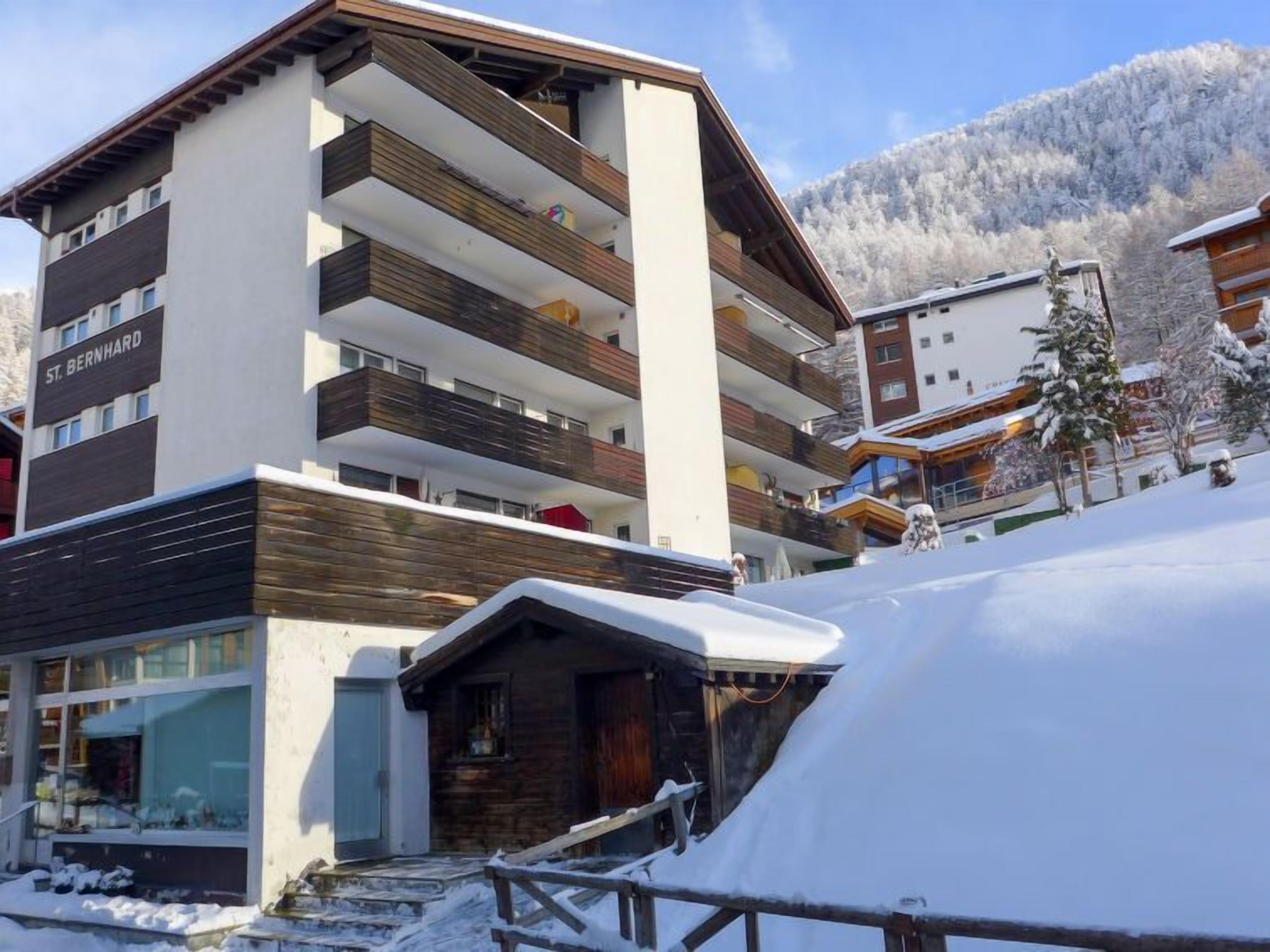 A multi-story hotel with a modern design, featuring balconies and a ski resort backdrop.