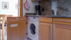 A compact kitchen with a built-in washer and dryer, wooden cabinets, and a marble countertop. - St. Bernhard by Interhome (Zermatt)