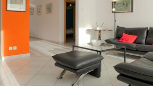 A modern living room with a black leather sofa, a glass coffee table, and a black leather ottoman. There are framed pictures on the walls and a lamp on a side table. - St. Bernhard by Interhome (Zermatt)