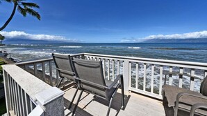 A deck with two chairs overlooking a beach with waves and a clear sky.