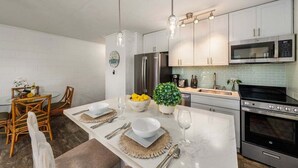 A modern kitchen with white cabinets, stainless steel appliances, and a dining area with a glass table and chairs.