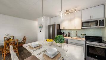 Een moderne keuken met witte kastjes, roestvrijstalen apparatuur en een eethoek met een glazen tafel en stoelen.