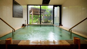 A hot spring bath with wooden benches and a view of a traditional building through a glass door. - Appi Kogen Mori no Hotel (Hachimantai)