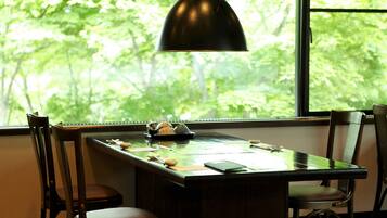 A dining table with chairs, a pendant light, and a window with a view of trees.