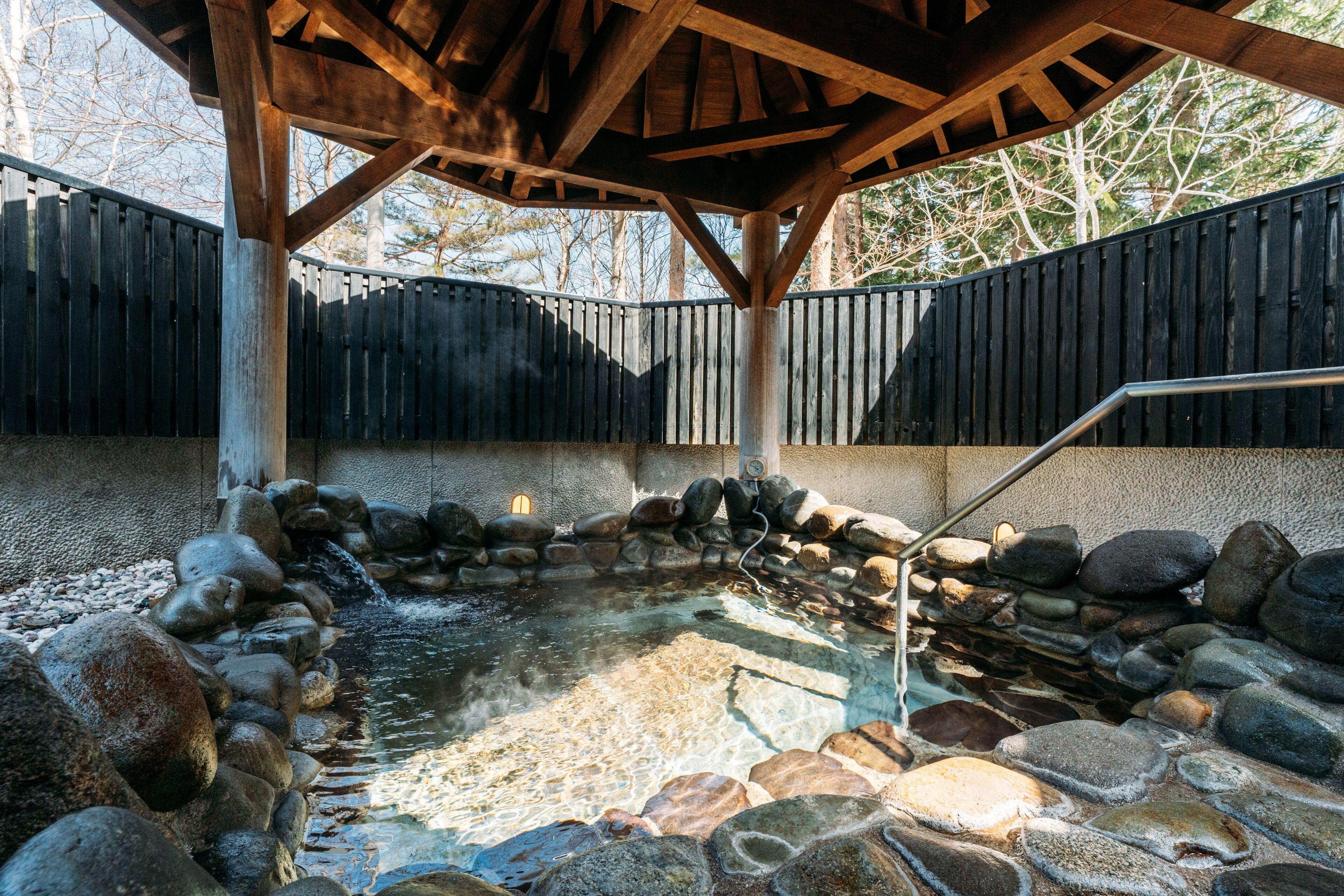 A hot spring area with a wooden deck, stone seating, and a stone wall surrounding the water.