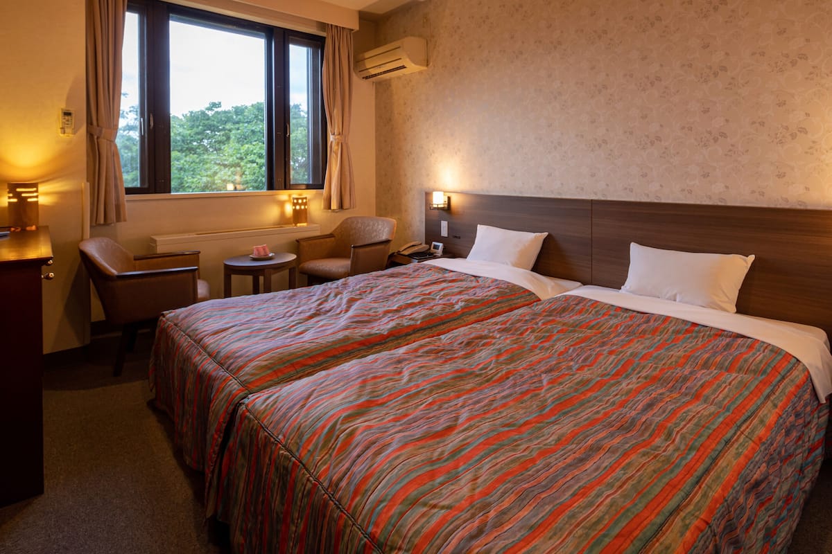 Een hotelkamer met twee bedden, een bureau, een stoel, een tafeltje en een raam met gordijnen.