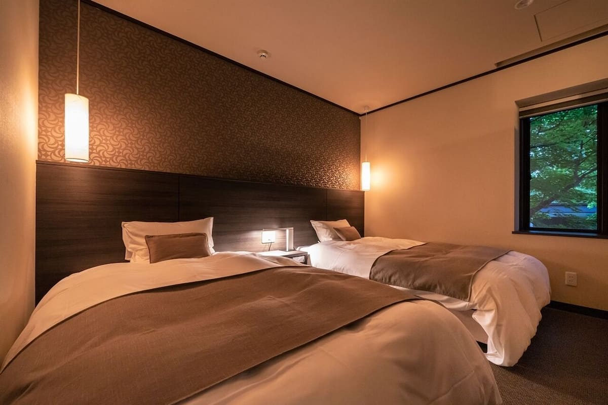 Een hotelkamer met twee bedden, een hoofdeinde, een raam met uitzicht en een wandlamp.
