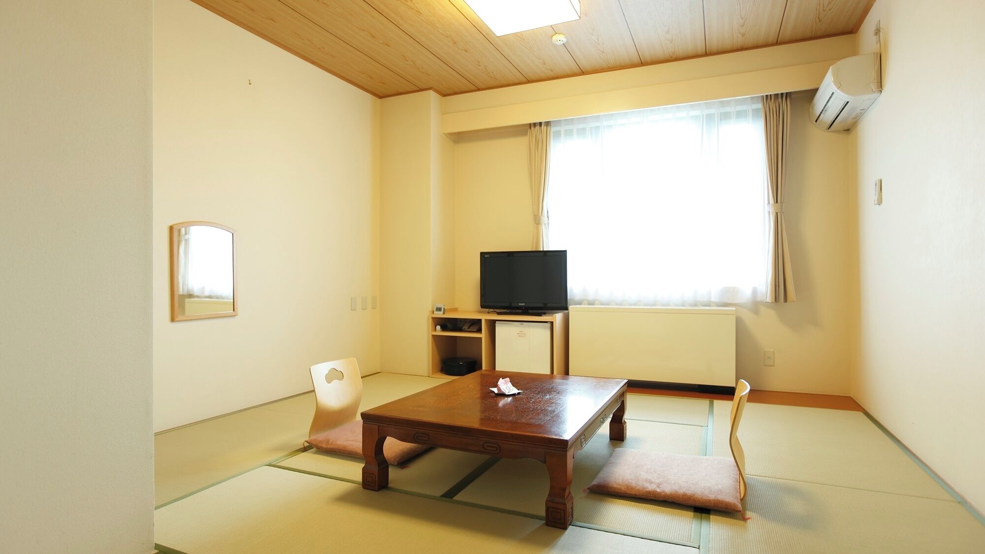 A room with tatami flooring, a wooden table, a television, a small refrigerator, and a window with curtains.