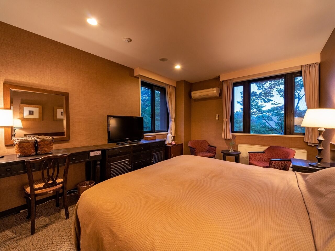 Une chambre d’hôtel avec un grand lit, un bureau avec une télévision, une chaise et une fenêtre avec des rideaux.