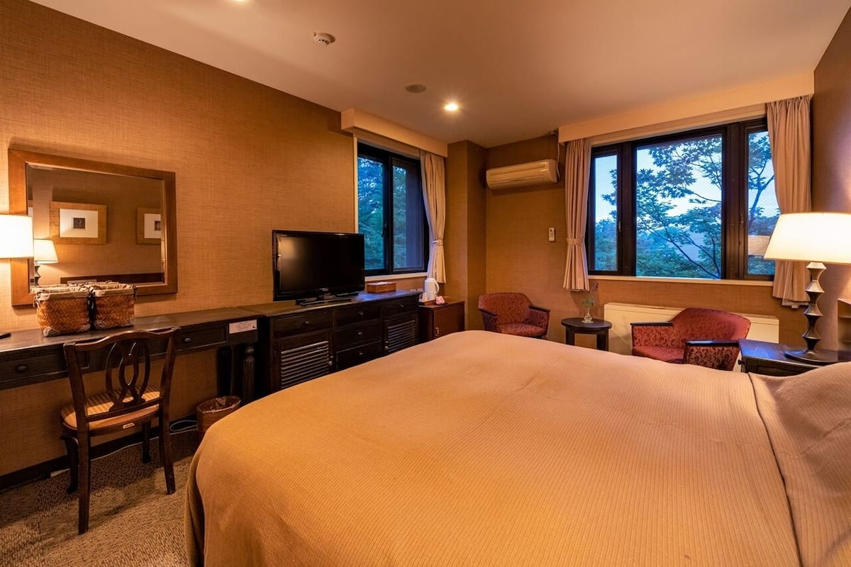 Una habitación de hotel con una cama grande, un escritorio con televisor, una silla y una ventana con cortinas.