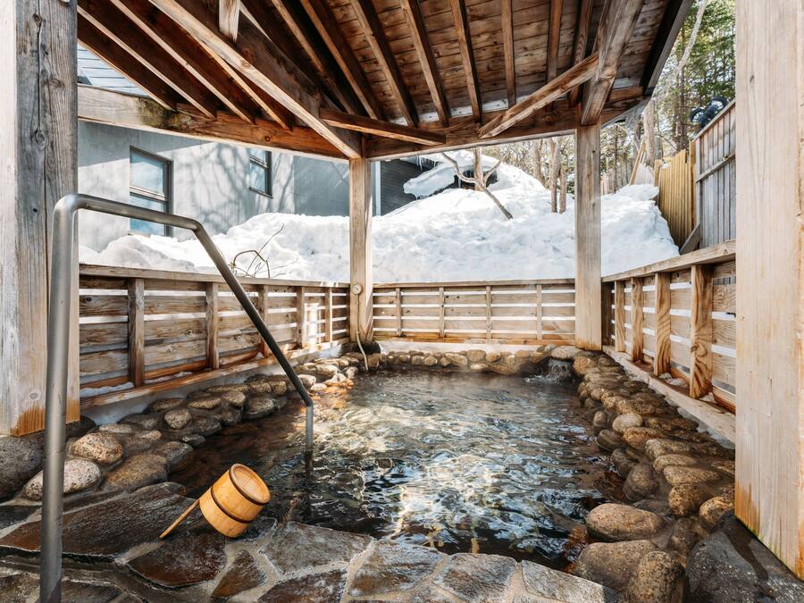 A wooden hot spring bath with a stone floor, surrounded by snow.