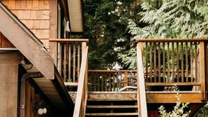 A wooden staircase leading to a deck with a dog sitting at the bottom.