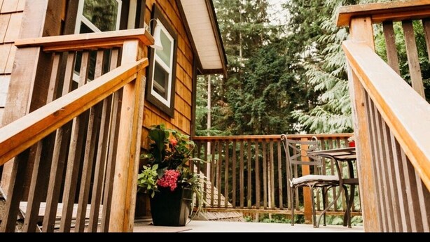 A wooden cabin with a deck, surrounded by trees.