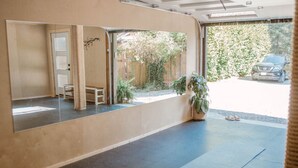 A room with a large mirror, a small table, a potted plant, and a view of a car and greenery outside.