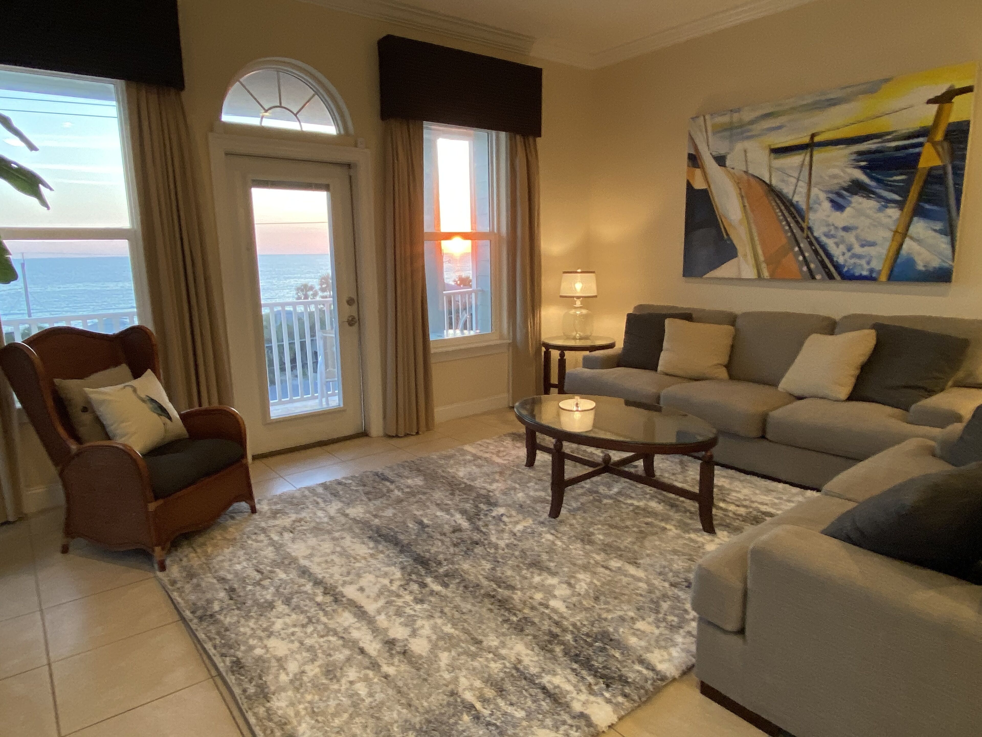 A living room with a view of the ocean, a sofa, a chair, and a lamp.