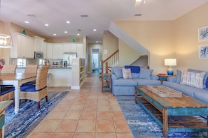 A spacious living area with a dining table, sofa, and coffee table, connected to a kitchen with white cabinets and a microwave.