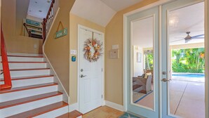 Una escalera con barandal de madera, una puerta blanca adornada con un adorno y una puerta de cristal que da al exterior.