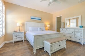Quarto com cama, mesas de cabeceira, um banco, cômoda e ventilador de teto.