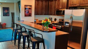 Una cucina moderna con isola centrale, sgabelli da bar, frigorifero e pensili in legno.