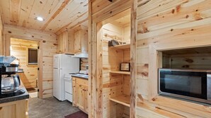 Interior de uma cabana de madeira com cozinha, incluindo fogão, geladeira e armários.