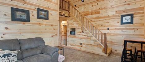 Ein Interieur einer Holzhütte mit Holzwänden, einem grauen Sofa, einem kleinen Tisch und einer Treppe.