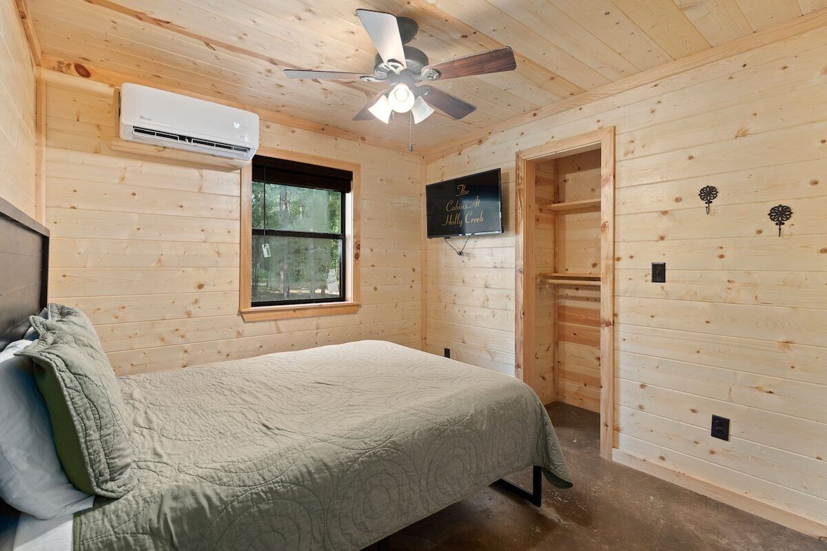 Een houten kamer met een bed, een plafondventilator, een airconditioner, een raam en een deur.