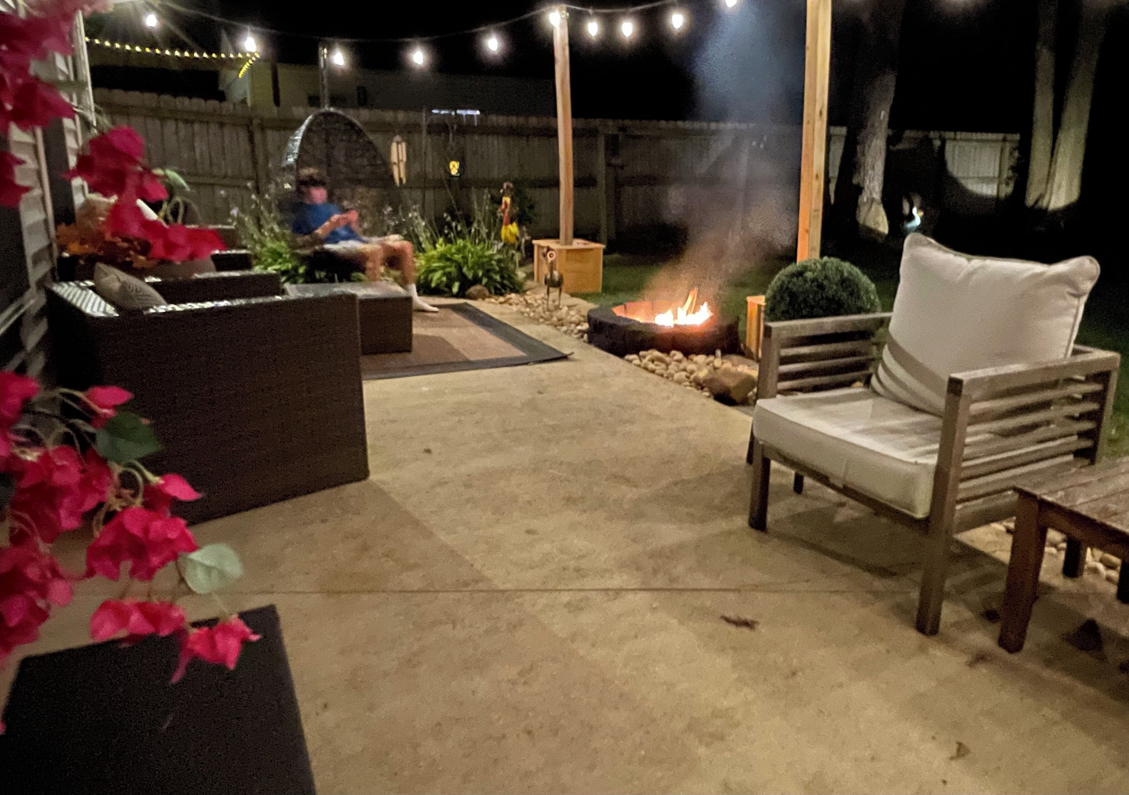 An outdoor patio area with a fire pit, seating, and string lights.