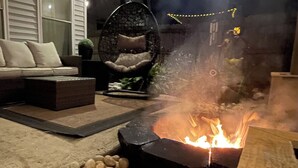 A fire pit surrounded by rocks, a sofa, and a hanging chair in an outdoor setting. - Cozy Home with LOTS of space- Less than 1 mile to ISU & IWU, 5 miles to airport (Normal)