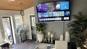 A modern living room with a flat-screen TV mounted on the wall displaying various channels and apps. There is a dining table with chairs and a decorative centerpiece. - Cozy Home with LOTS of space- Less than 1 mile to ISU & IWU, 5 miles to airport (Normal)