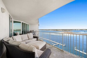 Un balcon avec un canapé en osier et une porte vitrée donnant sur un espace piscine.